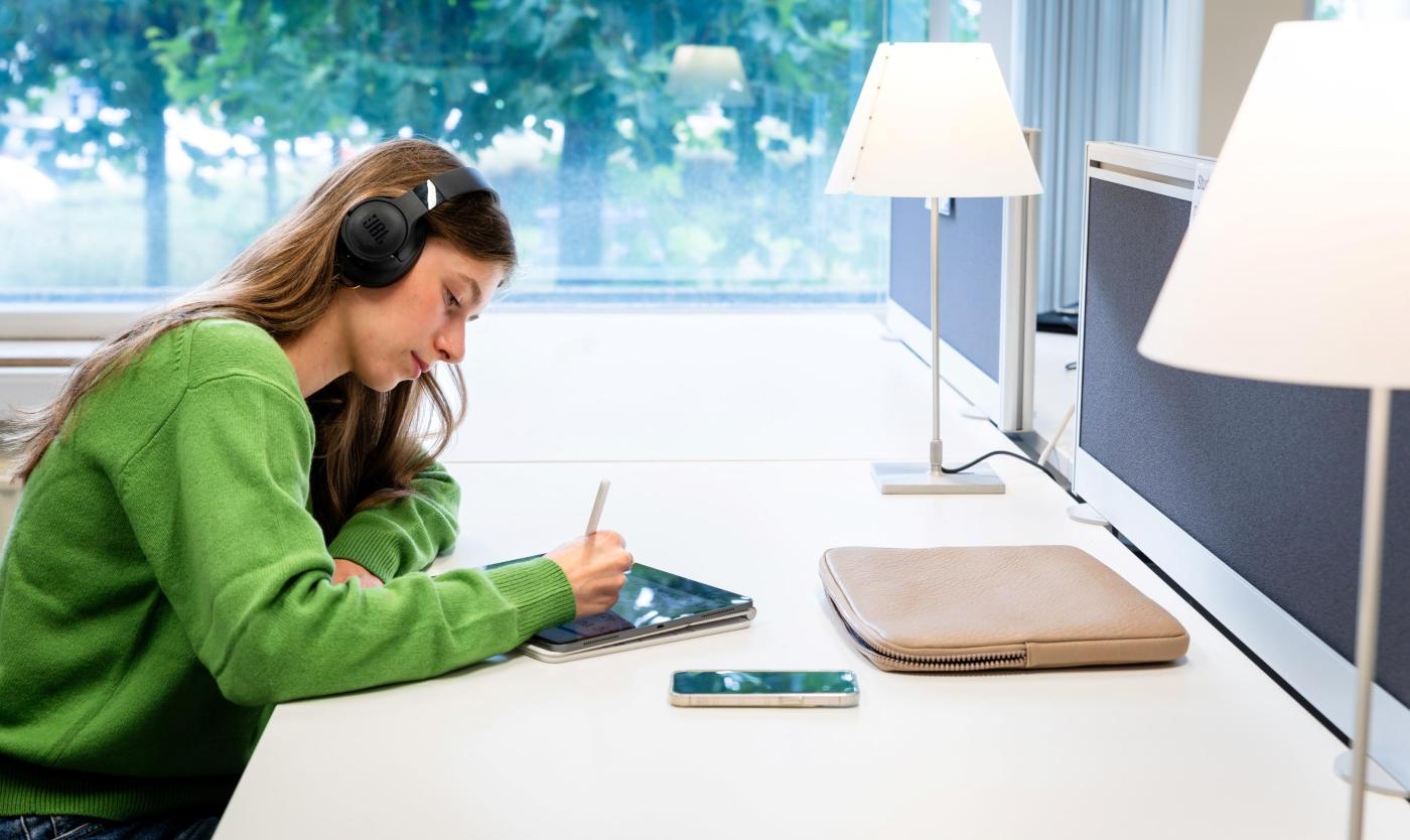 Student met hoofdtelefoon studeert in de bibliotheek op de Health Campus in Jette