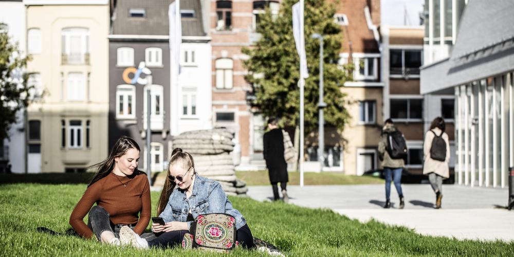 Studenten zitten op gras aan de IXY gebouwen op campus Etterbeek