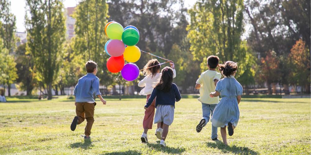 Kinderen lopen over grasveld met ballonnen